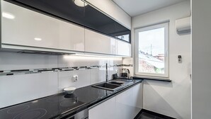 Una cocina moderna con encimera negra, electrodomésticos de acero inoxidable y una ventana con vistas a edificios.