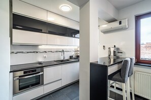 A modern kitchen with built-in appliances, a bar area, and a window with a view. - RentPlanet - Apartament Zamoyskiego (Kraków)