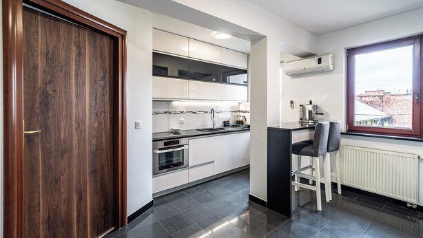 Una cocina moderna con armarios blancos, horno empotrado, encimera negra y ventana con vistas a edificios.