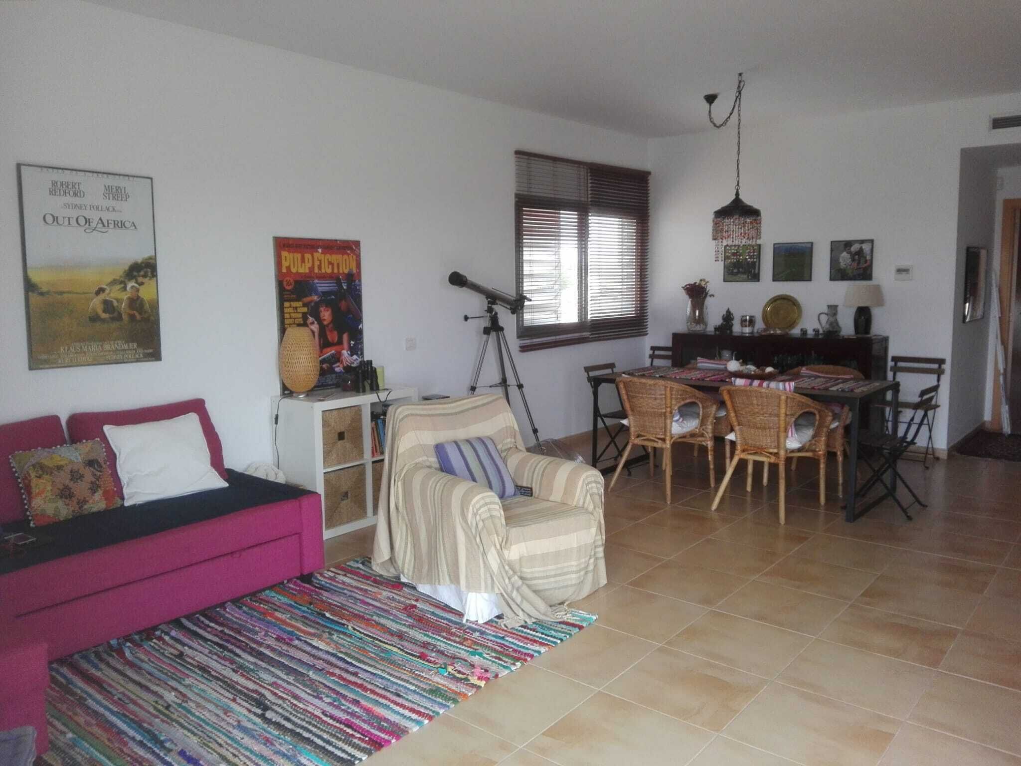 A living room with a sofa, armchair, dining table with chairs, a telescope, and a poster on the wall.