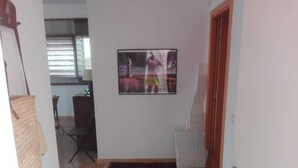 Un couloir avec un tableau encadré au mur, un tapis à motifs sur le sol, une chaise blanche et une porte.