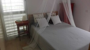 Une chambre à coucher avec un lit, une table de chevet, une lampe et une fenêtre avec des stores.