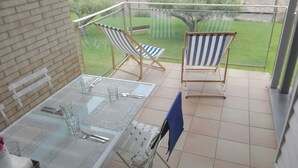 Un balcon avec une table en verre dressée pour deux personnes, deux fauteuils de jardin à rayures et une vue sur un paysage verdoyant.