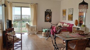 Un salon comprenant une table à manger, des chaises, un vélo, un canapé rose et un téléviseur.
