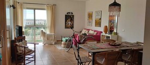 Un soggiorno con un tavolo da pranzo, sedie, una bicicletta, un divano rosa e una televisione.