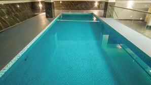 Una piscina interior con agua cristalina, rodeada de paredes de mármol y una barandilla de vidrio.