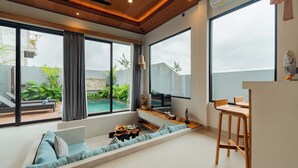 Ein modernes Wohnzimmer mit einer Couch, einem Holztisch und großen Fenstern mit Blick auf einen Swimmingpool und Grünflächen.