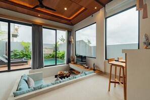 Ein modernes Wohnzimmer mit einer Couch, einem Holztisch und großen Fenstern mit Blick auf einen Swimmingpool und Grünflächen.