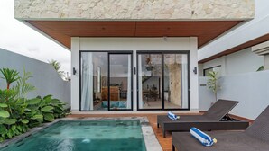 Ein moderner Poolbereich im Freien mit einer Steinmauer, Liegestühlen und einer Glastür zu einer überdachten Terrasse.