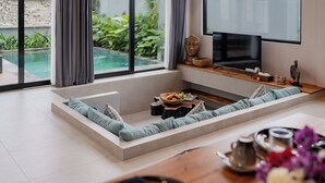 Ein modernes Wohnzimmer mit großem Fenster, einem Flachbildfernseher, einer integrierten Sitzecke und einem kleinen Pool, der durch das Fenster sichtbar ist.