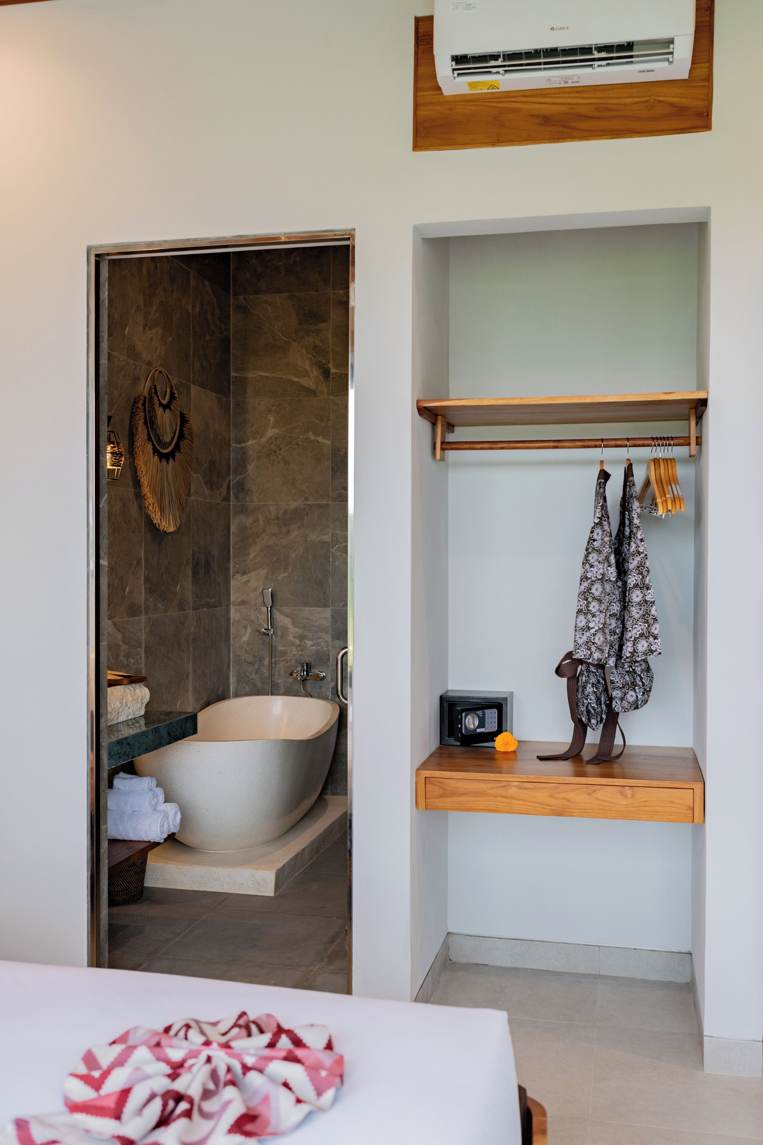 A modern bathroom with a freestanding bathtub, a wooden shelf with towels, and a wall-mounted air conditioner.