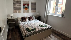 Un dormitorio con cama, mesitas de noche, adornos en la pared, una ventana y una lámpara colgante.