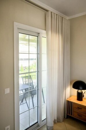 Ein Zimmer mit einer Schiebetür und einem Balkon, einem Holzkasten mit Schubladen und einer schwarzen Lampe auf dem Kasten.