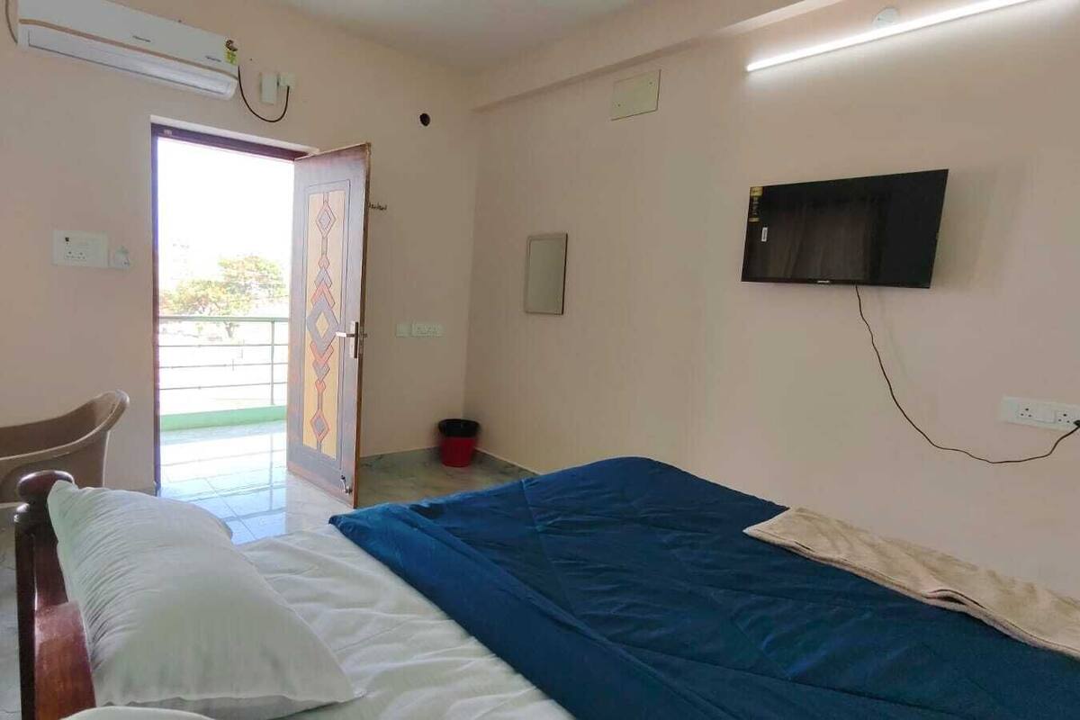 A room with a bed, a chair, a television, and a door leading to a balcony.