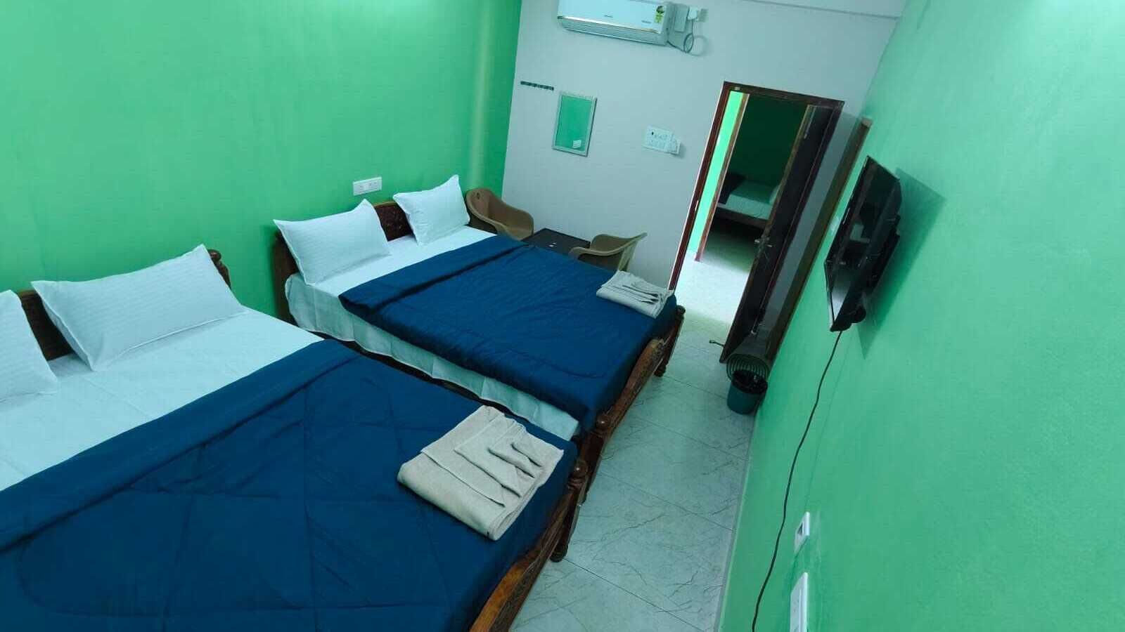 A room with two beds, a chair, a mirror, and a wall-mounted heater.