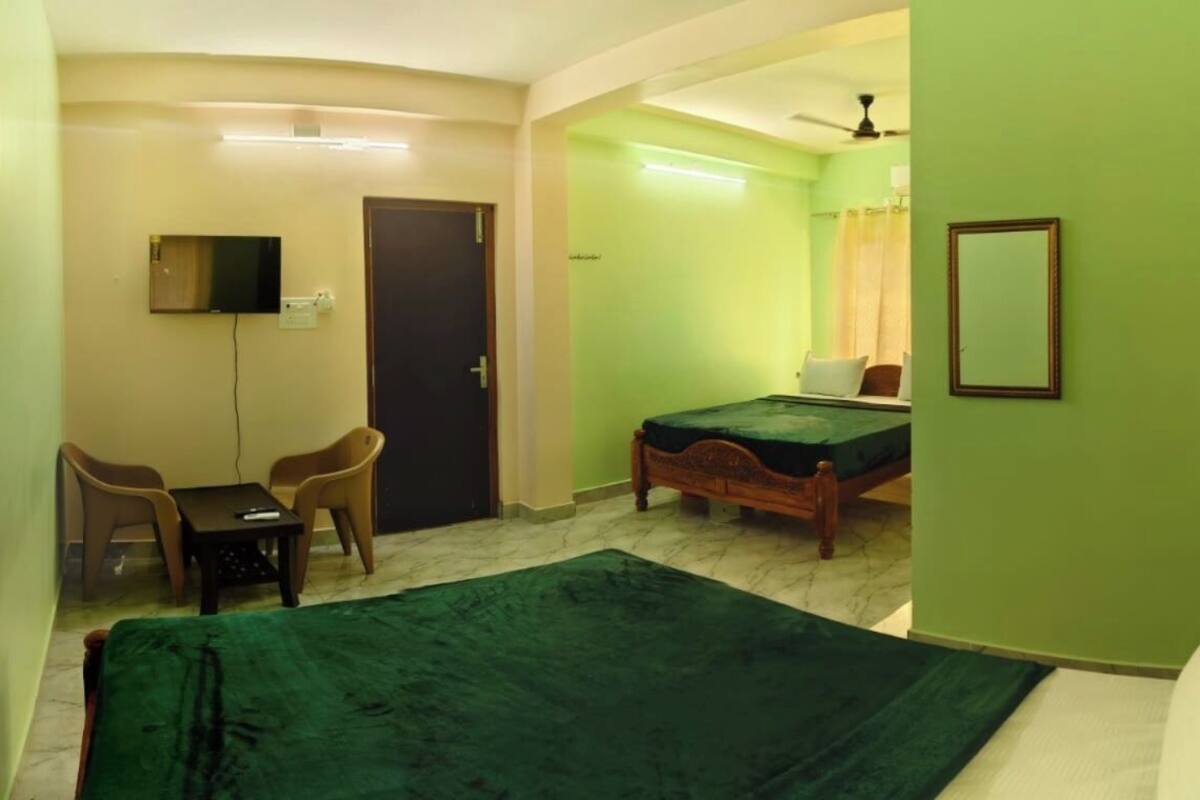 A room with a bed, a desk with chairs, a television, and a door.