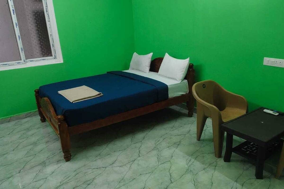 A room with a bed, a table, two chairs, a window, and a power outlet.