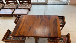 A wooden dining table with matching chairs, a tiled floor, and a view through a glass door. - Atithi Sevalay (Varanasi)