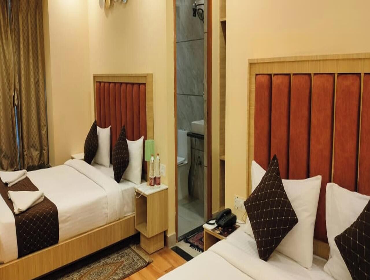 Hotellihuone, jossa on kaksi sänkyä, yöpöytä lampun kanssa ja kylpyhuone, joka on näkyvissä lasiovesta.
