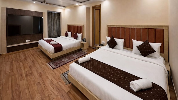 A hotel room with two beds, a TV, a ceiling fan, and a wooden floor. - Atithi Sevalay (Varanasi)