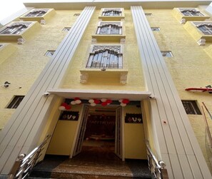 Um edifício de vários andares com uma entrada central, uma escadaria que leva à entrada e um banner com o texto '2016 HAPPY NEW YEAR'.