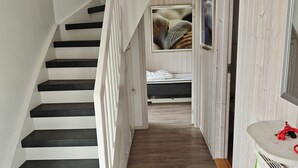 Escada que leva a um quarto com uma cama, mesa de cabeceira e TV fixada na parede.