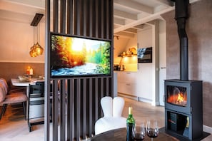 A modern living room with a TV mounted on a wooden panel, a fireplace, and a dining area with a table and chairs. - Casa Vida Verde - Luxury cottage by water & nature (Gramsbergen)