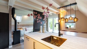 A modern kitchen with a built-in sink, a dining area with a table and chairs, and a decorative vase with flowers. - Casa Vida Verde - Luxury cottage by water & nature (Gramsbergen)
