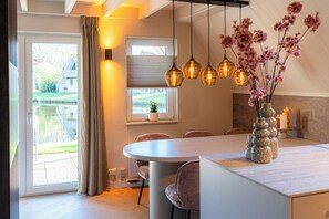 A modern kitchen with a round island, pendant lights, and a vase with flowers. - Casa Vida Verde - Luxury cottage by water & nature (Gramsbergen)