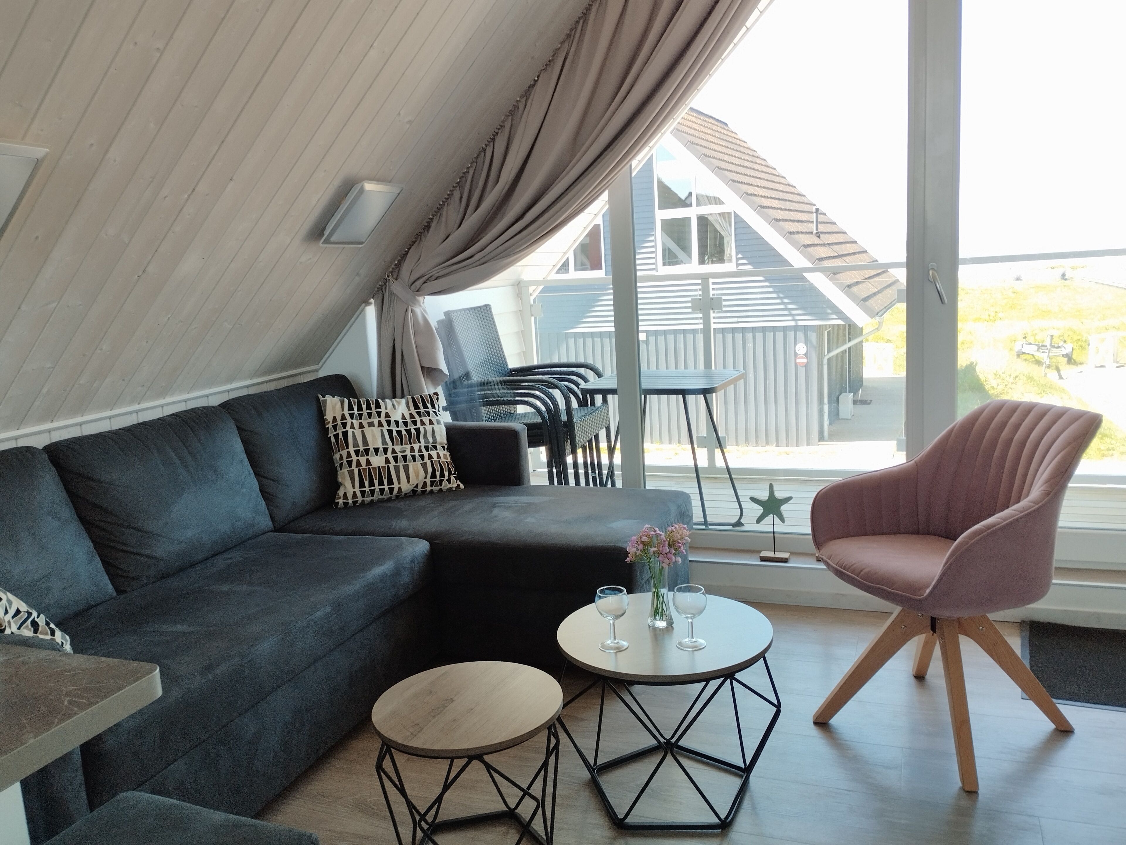 A modern living area with a sofa, a round coffee table, a pink chair, and a view of the outside.