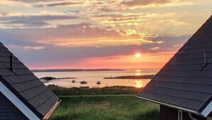 A sunset view from a building with a sloped roof, a grassy foreground, and a body of water in the distance. - "Strandgut" Marina Wendtorf holiday home by the beach with sea view (Wendtorf)