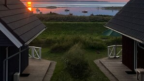 A sunset view from a cabin with a wooden deck and a grassy foreground. - "Strandgut" Marina Wendtorf holiday home by the beach with sea view (Wendtorf)