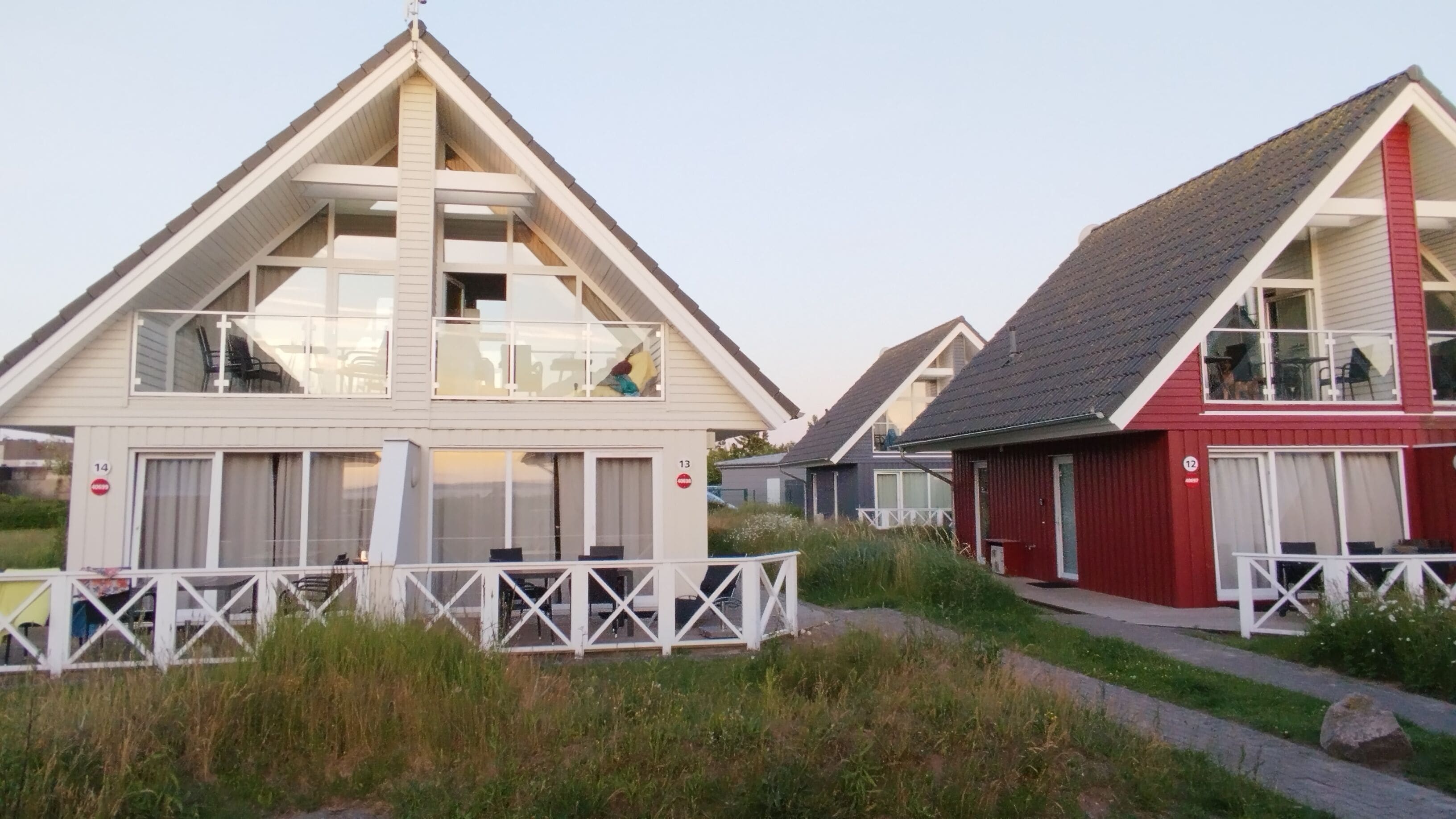 A row of beach houses with white and red exteriors, each with a balcony and a small deck area.