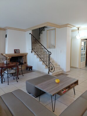 A living room with a fireplace, a dining table, a sofa, a staircase, and a hallway. - House T4 center Bastia - terrace, comfort and ideal location (BASTIA)
