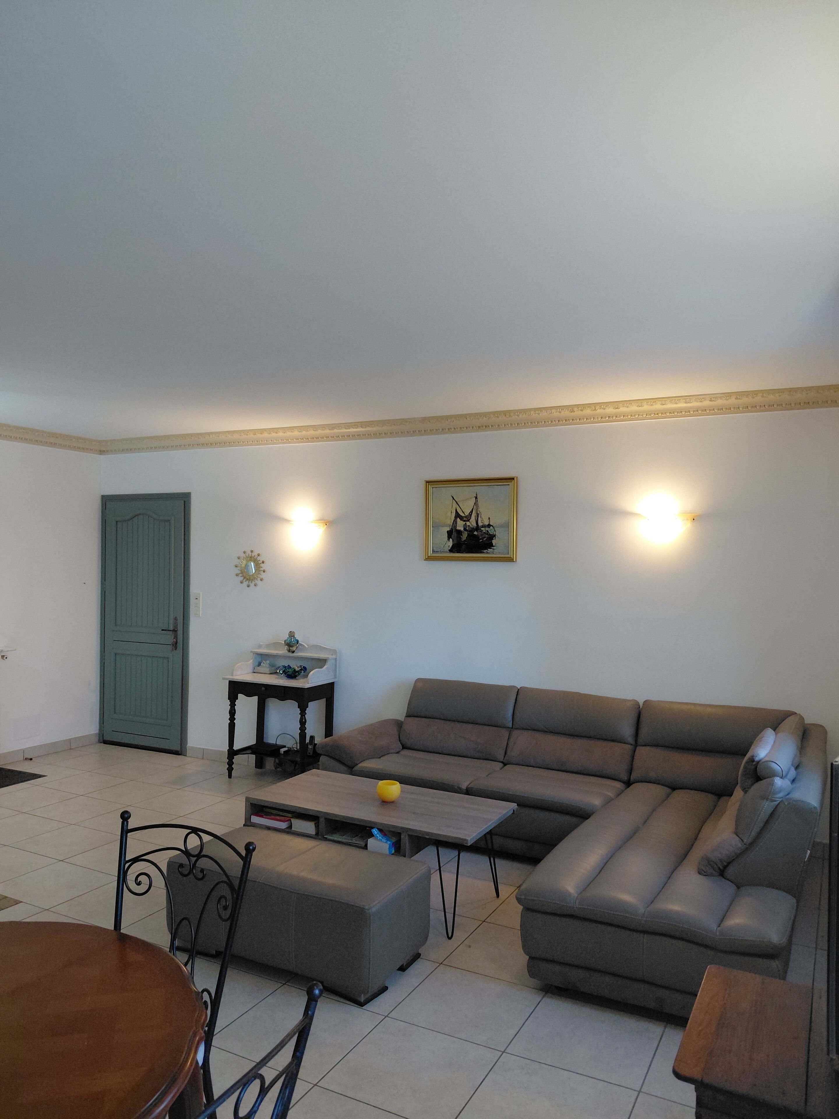A living room with a sofa, a coffee table, a dining table with chairs, a small side table, and a door.