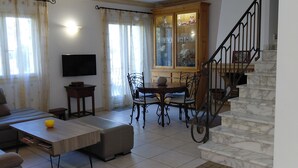 Ein Wohnzimmer mit Sofa, Couchtisch, Esstisch mit Stühlen, einer Treppe und einem an der Wand befestigten Fernseher.