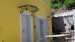 Ein gelbes Gebäude mit einer Terrassenfläche, einer weißen Tür und einem Tisch mit Stühlen.