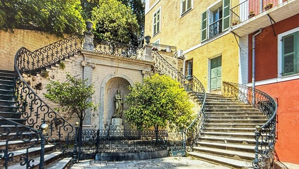 Eine Steintreppe mit schmiedeeisernen Geländern, einer Statue und einem Baum in einem Innenhof.