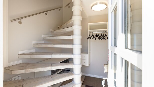 Eine Wendeltreppe mit Handlauf, ein Kleiderschrank mit aufgehängter Kleidung und eine Tür zu einem anderen Raum.