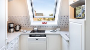 Eine Küche mit weißen Schränken, einem Geschirrspüler, einer Kaffeemaschine und einem Fenster mit Blick auf Gebäude.