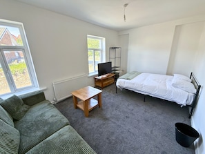A bedroom with a bed, a TV, a small table, a sofa, and a radiator. - 6 Bedroom House for up to 10 People (Merthyr Tydfil)