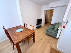 A dining area with a wooden table and chairs, a television on a stand, and a green sofa in a living room. - 6 Bedroom House for up to 10 People (Merthyr Tydfil)
