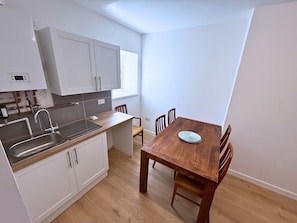 A compact kitchen with a sink, cabinets, and a dining table with chairs. - 6 Bedroom House for up to 10 People (Merthyr Tydfil)