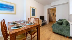 Un coin repas avec une table en bois dressée pour quatre personnes, des chaises et un tableau accroché au mur.