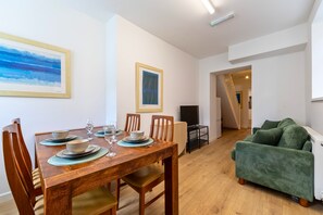 Un comedor con una mesa de madera preparada para cuatro personas, sillas y un cuadro en la pared.