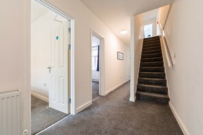 A hallway with carpeted flooring, white walls, a door with a sign, and a staircase with carpeted steps. - 6 Bedroom House for up to 10 People (Merthyr Tydfil)