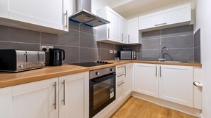 Une cuisine moderne avec des meubles blancs, une hotte en acier inoxydable, un grille-pain, une machine à café, un four à micro-ondes et un évier.