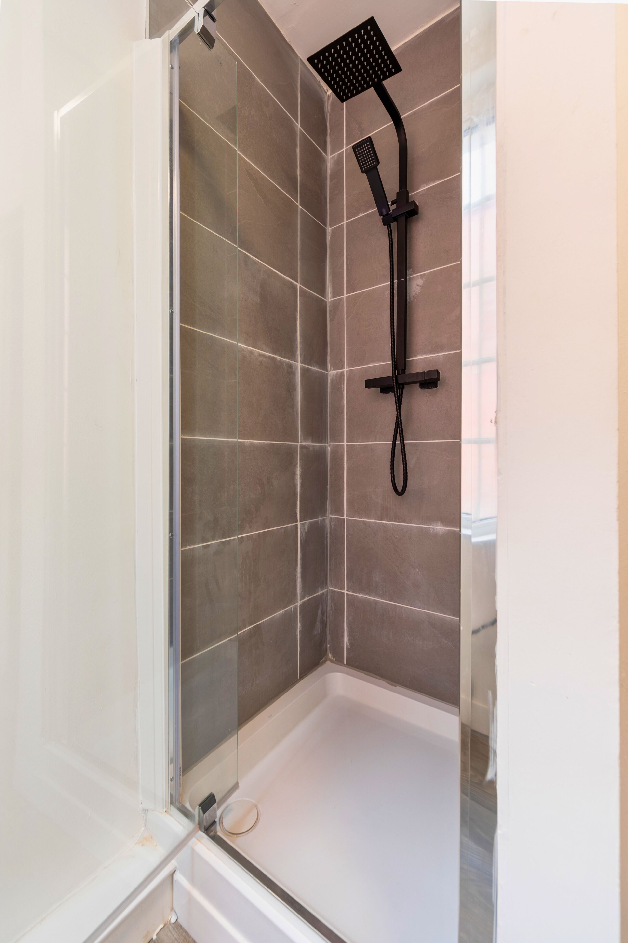 Cabina de ducha con puerta de vidrio, ducha de mano y panel de control en la pared.