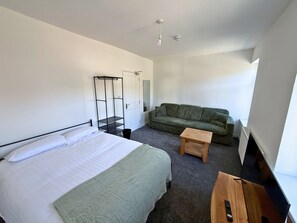 Et hotelværelse med en seng, en grøn sofa, et lille træbord og et tv-skab.