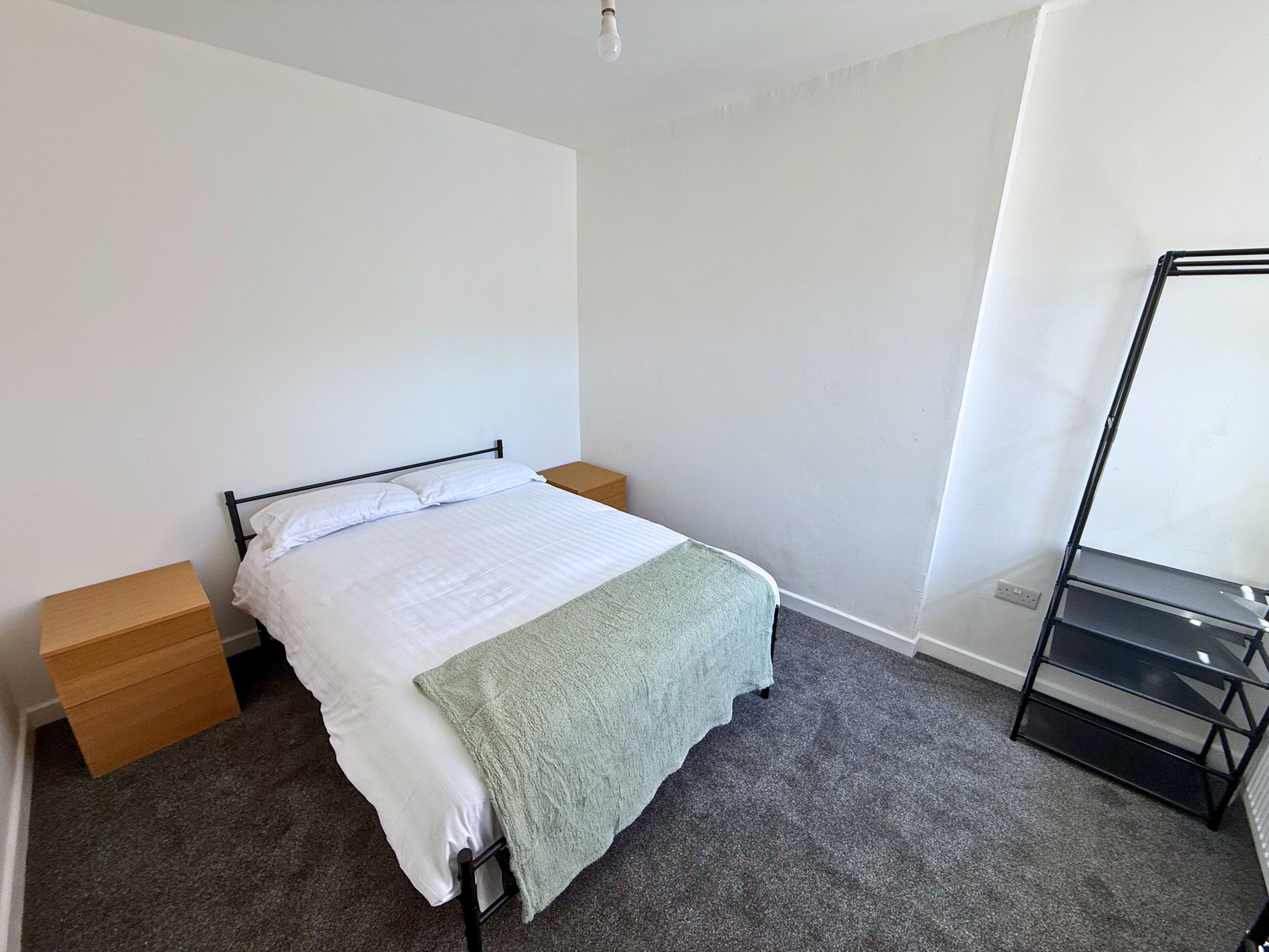 Une chambre à coucher comprenant un lit, une table de chevet, une commode, un miroir et un sol recouvert d’une moquette.